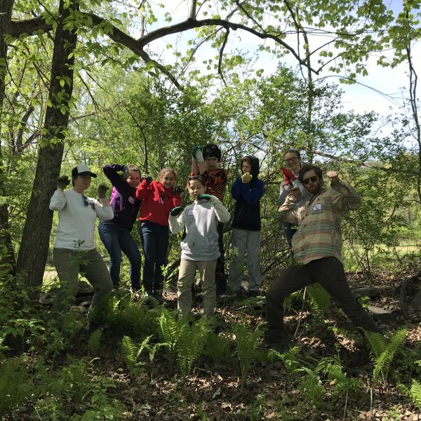 middle school students pose in front of the wooded area where they just removed invasive plants