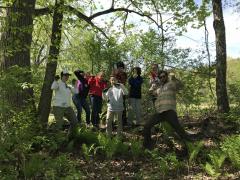 middle school students pose in front of the wooded area where they just removed invasive plants